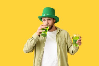 Sarı arka planda bira bardaklarıyla cüce şapkalı genç adam. Aziz Patrick Günü kutlaması