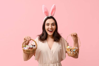 Duygusal genç bir kadın pembe arka planda dekoratif kozmetik sepetleri tutuyor.