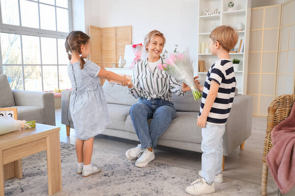 Маленькие дети приветствуют бабушку подарками дома. Международный женский день