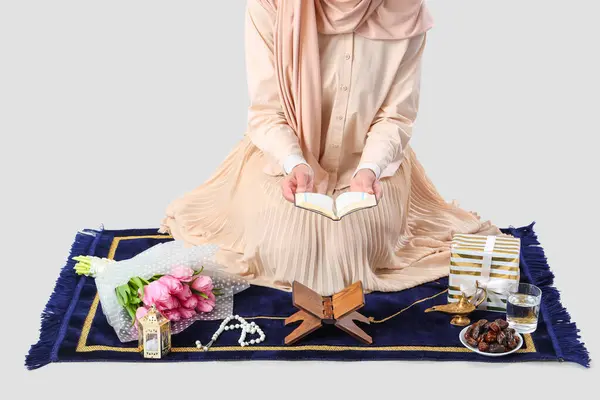 Muslim woman sitting on prayer mat with Koran and Ramadan symbols on white background