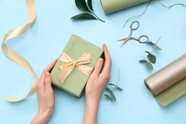 Weibliche Hände Mit Geschenkkarton Geschenkpapier Und Blättern Auf Blauem Hintergrund — Stockfoto