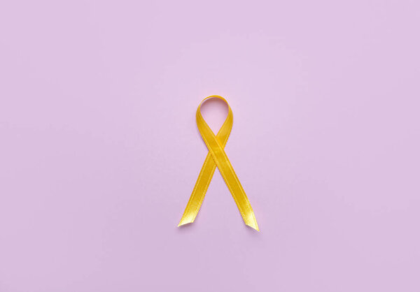 Golden ribbon on lilac background. Childhood cancer awareness concept