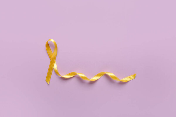 Golden ribbon on lilac background. Childhood cancer awareness concept