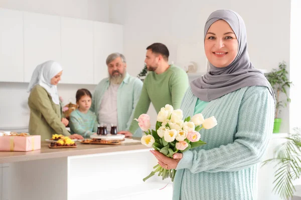 Mature Muslim woman with tulips and her family in kitchen. Ramadan celebration