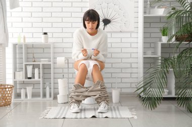 Hamilelik testi olan genç bir kadın evdeki klozette oturuyor.