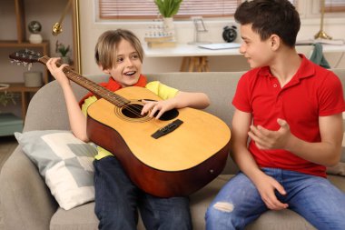 Küçük çocuk ve kardeşi evde gitar çalıyorlar.