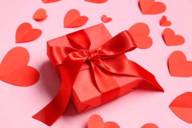 Hediye kutusu ve pembe arka planda kırmızı kağıt kalpler. Sevgililer Günü kutlaması