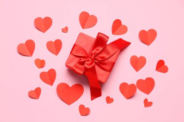 Hediye kutusu ve pembe arka planda kırmızı kağıt kalpler. Sevgililer Günü kutlaması