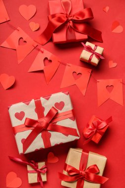 Kırmızı arka planda kağıt bayraklardan yapılmış çelenk ve kalplerden oluşan hediye kutuları. Sevgililer Günü kutlaması