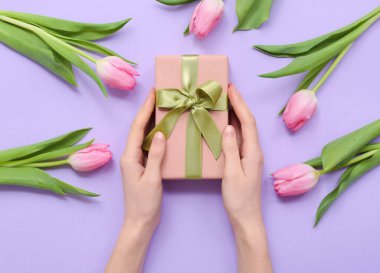 Hediye kutusu olan kadın eller ve leylak arka planda güzel laleler. Uluslararası Kadınlar Günü