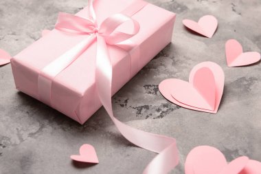 Gri arkaplanda Sevgililer Günü kutlaması için hediye paketi, kağıt kalpler ve kurdele, yakın plan.