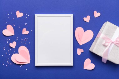 Mavi arkaplanda Sevgililer Günü kutlaması için boş çerçeveli, hediye kutusu ve kağıt kalpli kompozisyon