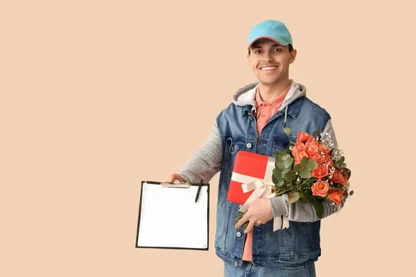 Male courier with bouquet of flowers, gift and clipboard on beige background