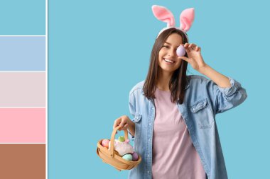 Tavşan kulaklı ve açık mavi arka planda Paskalya sepeti olan güzel bir genç kadın. Farklı renk desenleri