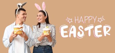 Tavşan kulaklı mutlu genç çift ve bej arka planda Paskalya pastaları. Paskalya bayrağı