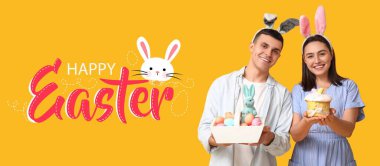 Tavşan kulaklı mutlu genç çift, sarı arka planda Paskalya sepeti ve pasta. Paskalya bayrağı