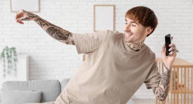 Evde cep telefonu dansı yapan dövmeli genç bir adam.