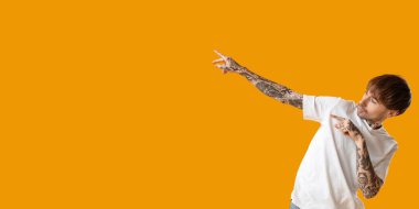 Genç dövmeli adam turuncu arka planda dans ediyor, mesaj için yeri var.