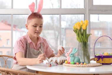 Mutfaktaki masada Paskalya yumurtası boyayan genç bir kadın.