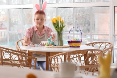 Mutfaktaki masada Paskalya yumurtası boyayan genç bir kadın.