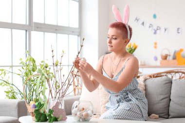 Evde Paskalya yumurtasıyla ağaç dallarını süsleyen genç bir kadın.