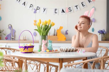 Tavşan kulaklı genç bir kadın Paskalya günü mutfakta masada oturuyor.