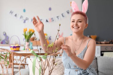Evde Paskalya yumurtasıyla ağaç dallarını süsleyen genç bir kadın.