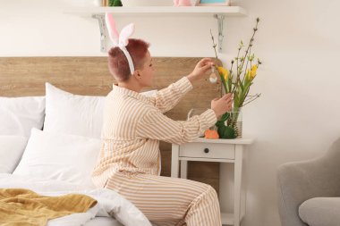 Yatak odasında Paskalya yumurtasıyla ağaç dallarını süsleyen genç bir kadın.