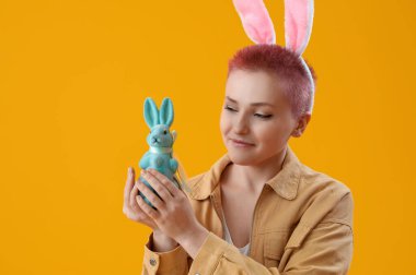 Tavşan kulaklı genç bir kadın ve sarı arka planda Paskalya tavşanı.