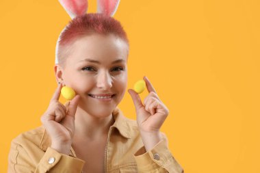 Tavşan kulaklı genç kadın ve sarı arka planda Paskalya yumurtaları, yakın plan.