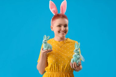 Tavşan kulaklı genç bir kadın ve mavi arka planda Paskalya tavşanları.
