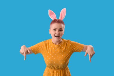 Tavşan kulaklı genç kadın mavi arka plandaki bir şeyi işaret ediyor. Paskalya kutlaması