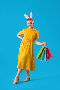 Tavşan kulaklı ve mavi arka planda alışveriş torbaları olan genç bir kadın.