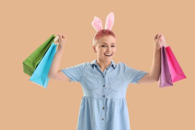 Tavşan kulaklı ve bej arka planda alışveriş torbaları olan genç bir kadın. Paskalya kutlaması