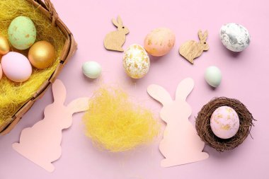 Paper rabbits and basket with Easter eggs on pink background