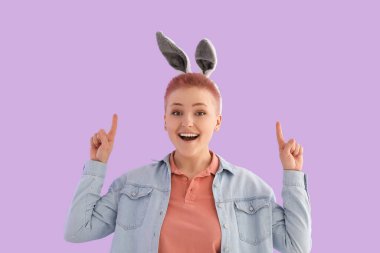 Tavşan kulaklı genç kadın leylak arkaplanındaki bir şeyi işaret ediyor. Paskalya kutlaması