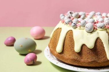 Lezzetli Paskalya pastası tabağı ve renkli arka planda boyanmış yumurtalar, yakın plan.