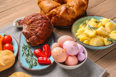 Tasty dishes and painted eggs for Easter dinner on wooden table