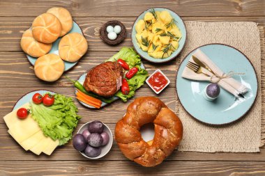 Tasty dishes and painted eggs for Easter dinner on wooden background