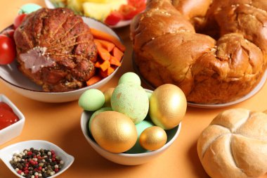 Bowl of painted eggs and tasty dishes for Easter dinner on color background, closeup
