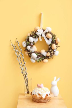 Vazoda söğüt dalları, Paskalya pastası, sarı duvarda tavşan ve çelenk olan masa.