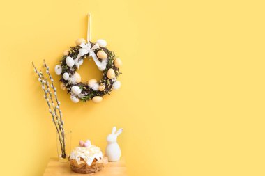 Vazoda söğüt dalları, Paskalya pastası, sarı duvarda tavşan ve çelenk olan masa.