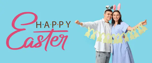 一对快乐的年轻夫妇 长着小兔子耳朵 戴着淡蓝色背景的节日花环 复活节贺卡横幅 — 图库照片