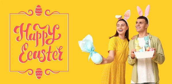 Šťastný Mladý Pár Králičími Ušima Dárkem Velikonočním Košíkem Žlutém Pozadí — Stock fotografie