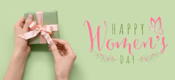 Female hands with gift box on green background.  Banner for International Women's Day