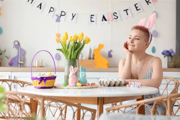 Tavşan kulaklı genç bir kadın Paskalya günü mutfakta masada oturuyor.