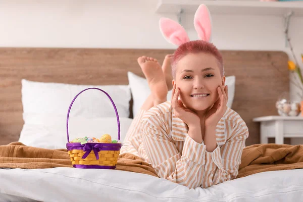 Tavşan kulaklı ve paskalya yumurtası sepeti olan genç bir kadın yatak odasında yatıyor.