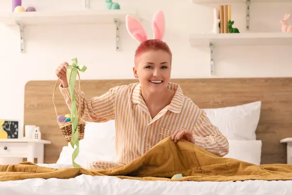 Young woman looking for hidden Easter egg under blanket in bedroom