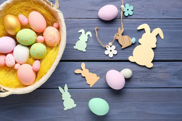 Basket with Easter eggs and paper rabbits on dark wooden background