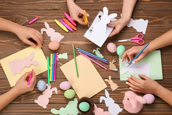 Women making Easter cards on wooden background, top view